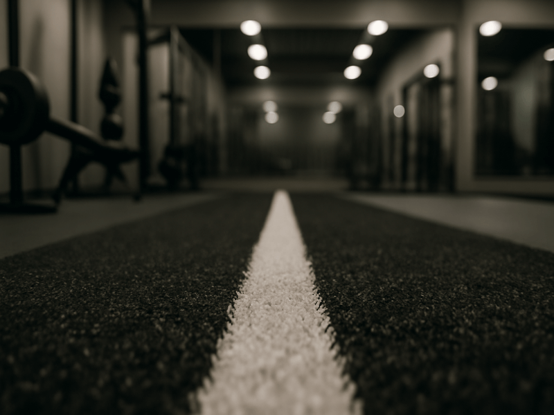 Wide shot of a modern gym with a green artificial turf sled track and custom markings